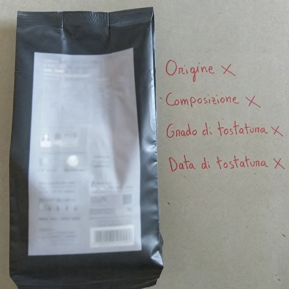 Una confezione di caffè con quattro voci annotate a mano — origine, composizione, grado di tostatura, data di tostatura — tutte barrate
